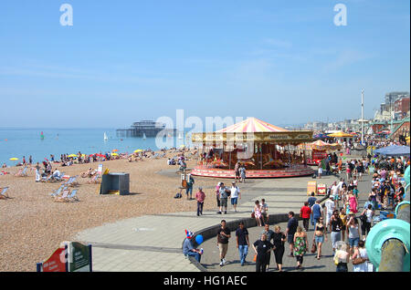 People on Brighton seafront, carousel, cafe and the remains of Old west pier, view from the promenade above. Stock Photo