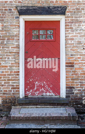An old red door is closed on a brick building. The paint is peeling and in decay.