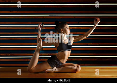 Young woman doing yoga exercises in dark studio. Health lifestyle concept. Stock Photo