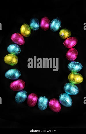 Colorful foil wrapped easter eggs laid out in the oval shape of an egg, on a black background. Stock Photo