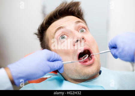 Scared young man at dentist office during teeth checkup Stock Photo
