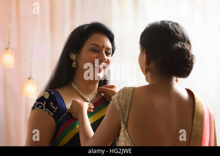 Daughter helping her mother in wearing necklace Stock Photo