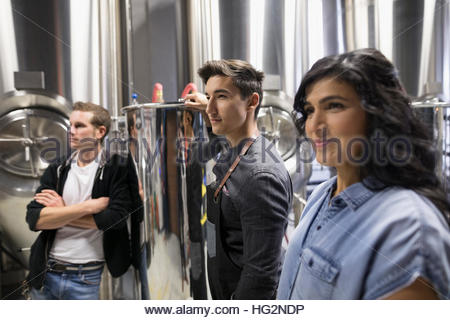 Confident brewers looking away next to vats in brewery
