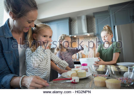 Mother and daughters baking in kitchen frosting cupcakes