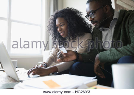 Couple with credit card and laptop paying bills online in living room