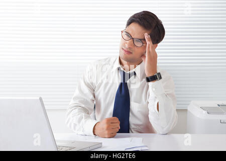 Young man looking frustrated and angry holding forehead sitting at office desk Stock Photo