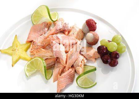 Salmon garnished with fruit: star fruit (carambola), limes, grapes and lychees Stock Photo