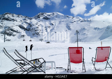 Red and white relaxing lounge chairs on snow in front of ski piste and lifts, in alpine winter resort of Les Arcs, France . Stock Photo