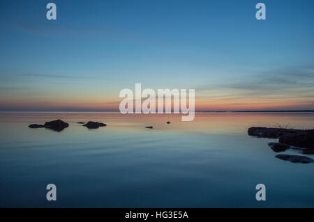A few small ripples around the rock silhouettes makes this peach and blue image of the water and sky restful Stock Photo