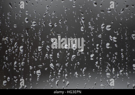 The image shows the pane only and background is darker and the raindrops lighter.   The rain drops are even over the glass. Stock Photo