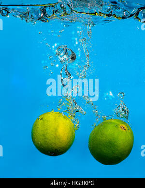 Lime splashing in water on blue background Stock Photo