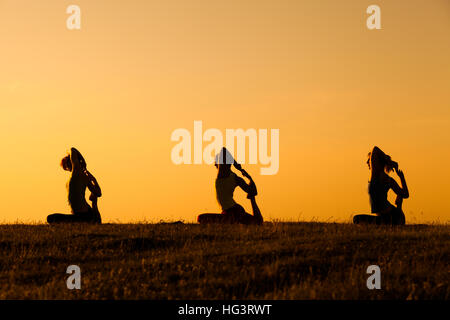 Three girl are practicing yoga at sunset. Stock Photo