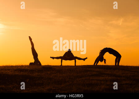 Three girl are practicing yoga at sunset. Stock Photo