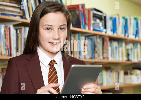 Girl Wearing School Uniform Using Digital Tablet In Library Stock Photo