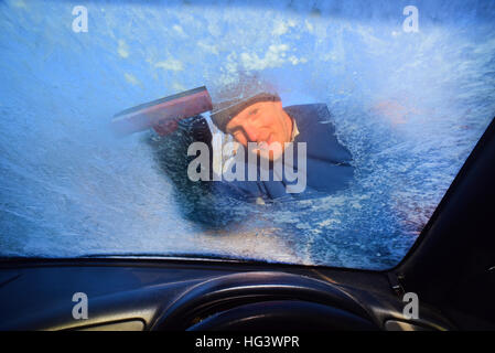 man using ice scraper to clear vehicle windscreen of thick ice uk Stock Photo