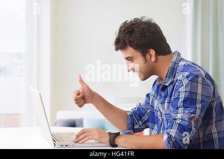 Smiling man showing thumbs up while using laptop computer Stock Photo