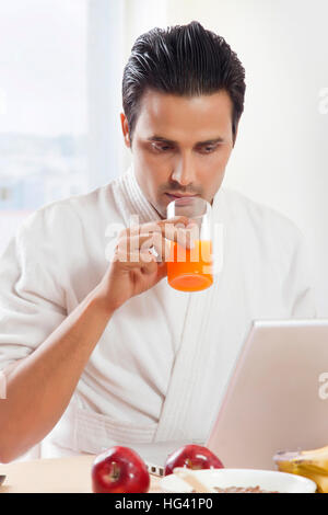 Man drinking juice while using laptop at breakfast table Stock Photo