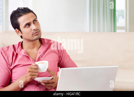 Young man drinking tea while using laptop Stock Photo