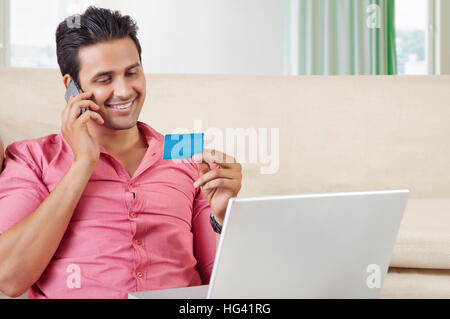 Young man at home paying bills with credit card on mobile phone Stock Photo