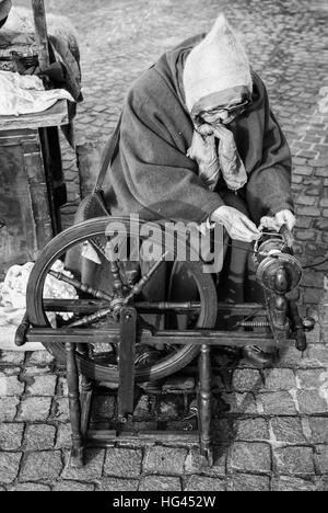 Trento, Italy - January 3, 2016: Elderly woman uses the cocoons of silkworms to spin using an old spinning wheel of wood. Stock Photo