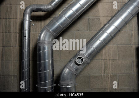 Industrial aluminium air conditioning pipes mounted on a breeze block wall. Stock Photo