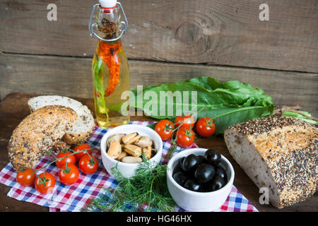 Black olives and mussels in ceramic bowls, fresh tomatoes, bread and bottle of olive oil with spices on wooden board. Mediterranean food on dark woode Stock Photo