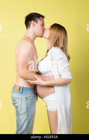 Beautiful young pregnant blonde girl and boy in studio shot on yellow background Stock Photo