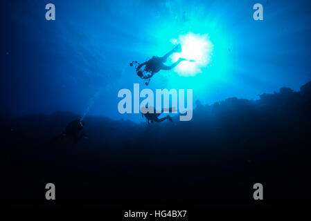 scuba divers swimming in sunshine along coral reef wall.  at Yap island Micronesia. Stock Photo