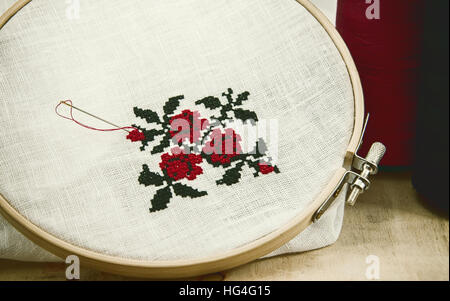 Hand embroidery cross-stitch flower ornament on a white fabric in the wooden embroidery frame red and black thread, vintage toning Stock Photo