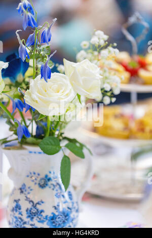 White roses with blue flowers and babys breath in a blue and white willow pattern porcelain jug  with tiered cake stand Stock Photo