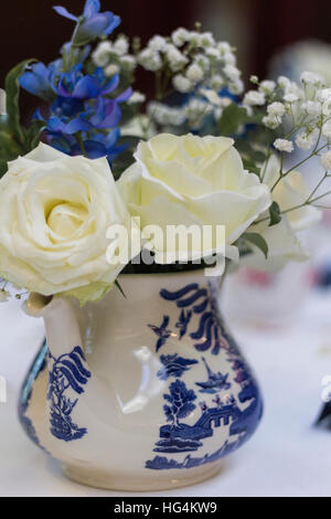 White roses with blue flowers and baby breath in blue and white transferware willow pattern porcelain jug, wedding centerpiece Stock Photo