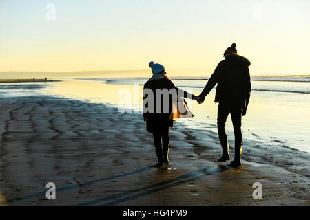 A young couple in love holding hands on a beach at sunset. Stock Photo