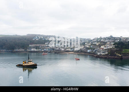 A tug boat travels down the River Fowey into the English Channel past the coastal village of Polruan in Cornwall, England Stock Photo