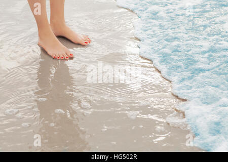 Woman's feet standing in surf at the beach Stock Photo