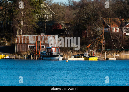 Ronneby, Sweden - January 2, 2017: Documentary of seaside lifestyle. Boats and a forklift outside a boathouse. Homes among the trees in the background Stock Photo