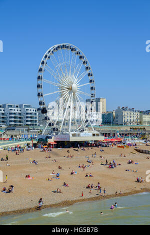 Ferris wheel in Madeira Drive with many people relaxing on the beach in front of Brighton pier, East Sussex, England, UK, removed in May 2016. Stock Photo