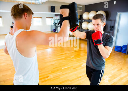 Confident Boxer Punching Bag Held By Instructor In Gym Stock Photo