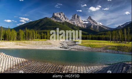 Three Sisters Mountain Peak, Green Forest Scenic Panoramic Landscape with Blue Skyline and Reservoir in Foreground.  Canmore, Alberta Canadian Rockies Stock Photo
