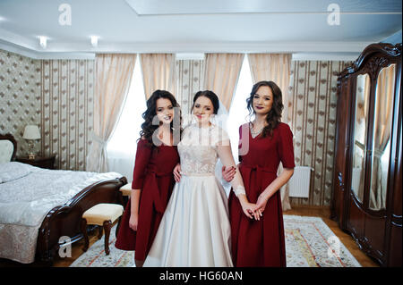 Bride with two amazing bridesmaids on red dress posed on room at wedding day. Stock Photo