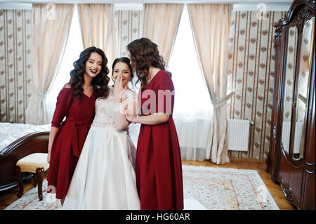 Bride with two amazing bridesmaids on red dress posed on room at wedding day. Stock Photo