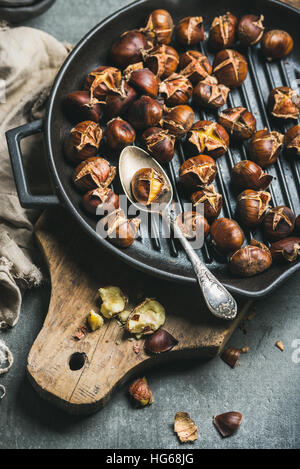 Roasted chestnuts in cast iron grilling pan over wooden board Stock Photo