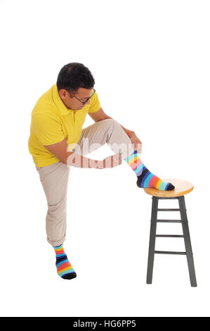 A middle age Hispanic man lifting up his leg on a chair and putting on his colorful socks, isolated for white background. Stock Photo
