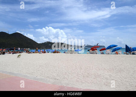 Sunbathers on the beach at Philipsburg, Saint Maarten. In the distance are cruise ships moored at their docks. Stock Photo