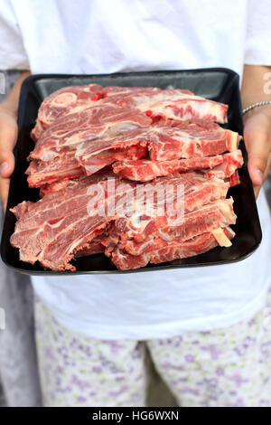 Hand holding Raw Lamb loin chops in plastic tray Stock Photo