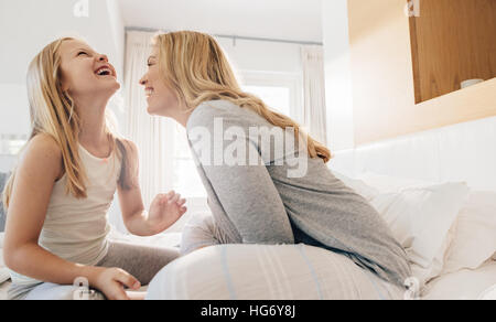 Shot of young woman and little girl sitting on bed and laughing. Mother and daughter enjoying in bedroom. Stock Photo