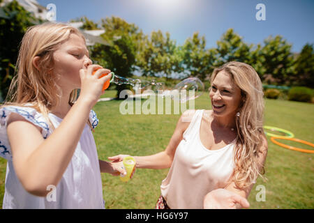 Little girl blowing soap bubbles with her mother smiling in park. Mother and daughter enjoying a day at park. Stock Photo