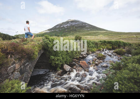 Lone walker stood on an old bridge in the poisoned Glen with a view of Mount Errigal. Glenveagh national park, County Donegal, I Stock Photo