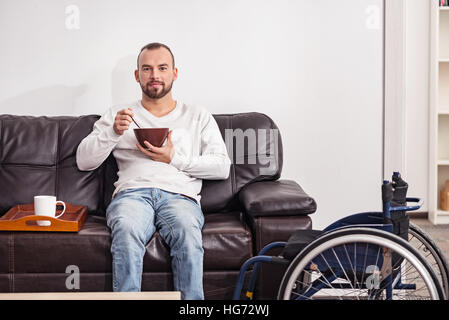 Positive disabled man having cereal in the living room Stock Photo