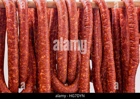 Row of smoked pork sausage in natural casings hanging on a wooden pole to dry Stock Photo