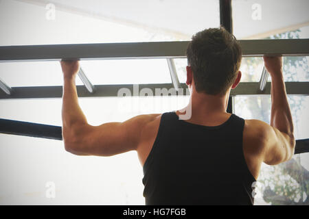 Athlete muscular fitness male model pulling up on horizontal bar in a gym Stock Photo